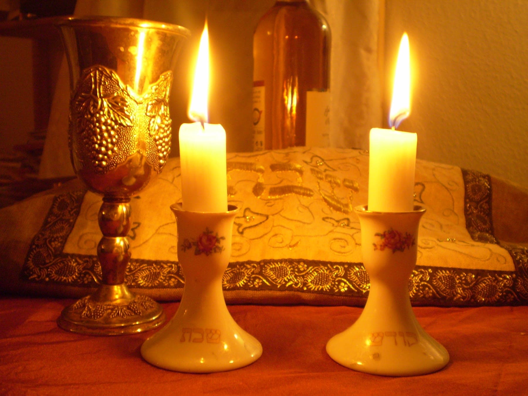 Two lit shabbat candles beside a silver kiddush cup.