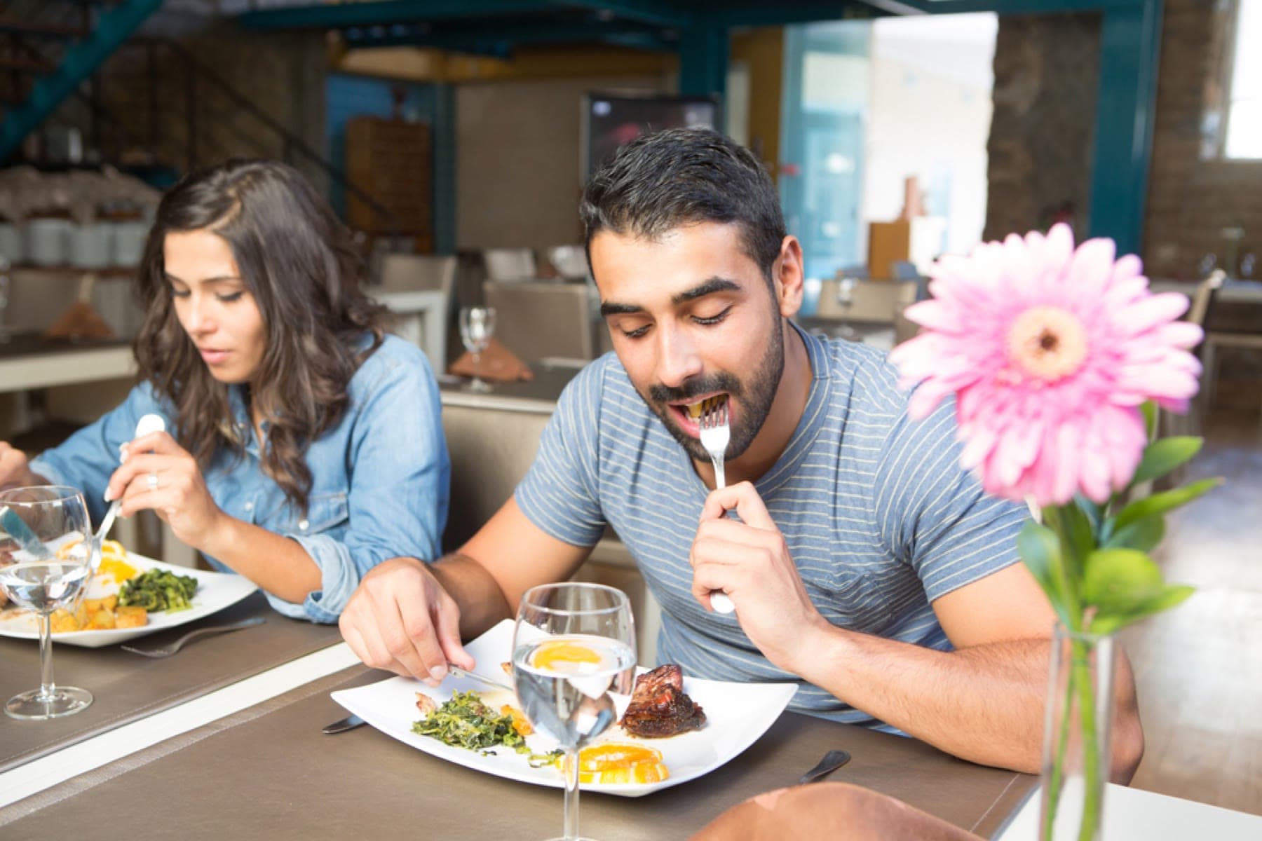 A couple eating together at a restaurant table, each with their own plate.